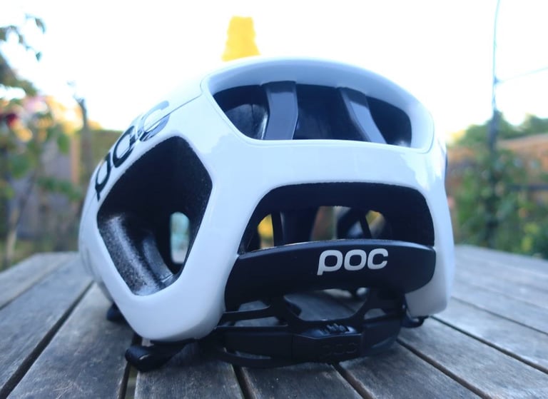 Rear view of the white POC Octal helmet on a wooden table, showing its large vents and dial retention system.