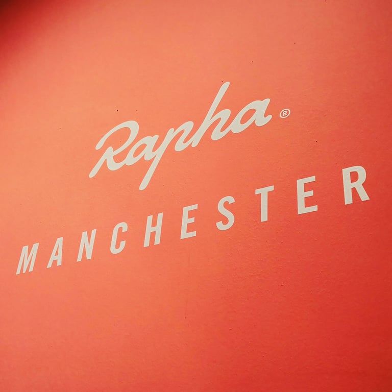 Rapha Manchester logo in white on an orange wall.