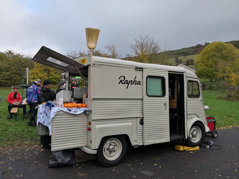 Vintage Rapha Broom Wagon van, broom on the roof, serving oranges and coffee at a Prestige Manchester checkpoint.