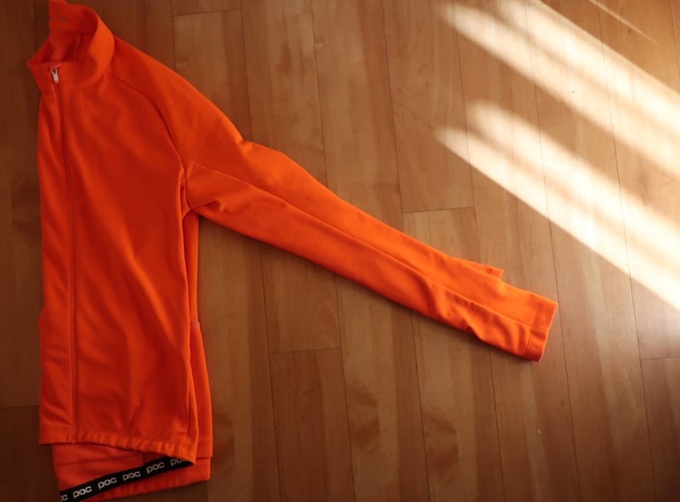 POC AVIP Ceramic Thermal Jersey laid flat on a wooden floor, its orange sleeve stretched out.
