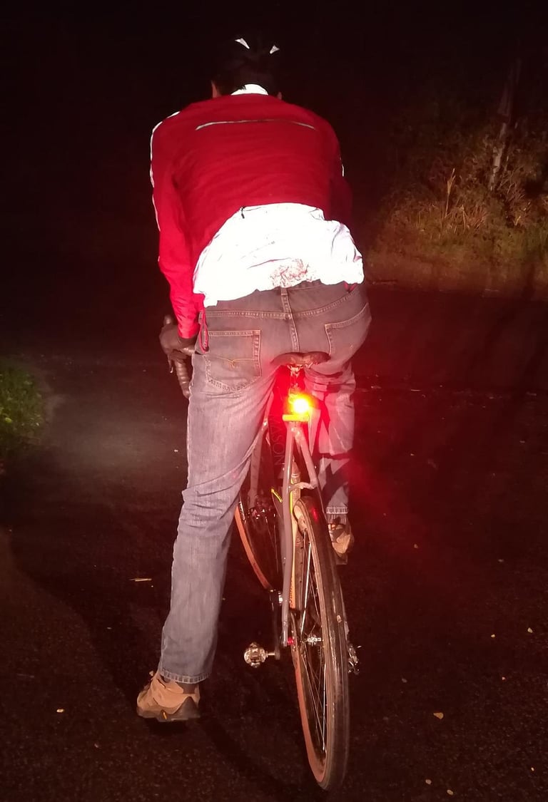 Rider cycles away on a dark lane in the Altura Nightvision Thunderstorm Jacket, rear light on and lower back reflecting.