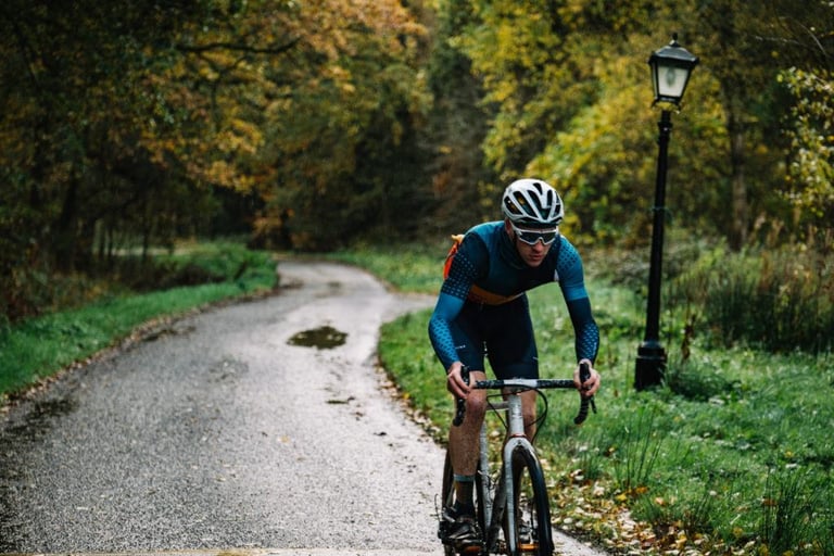 Rider in Victory Chimp Stampen kit climbs a wet lane through autumn woodland on a gravel bike.