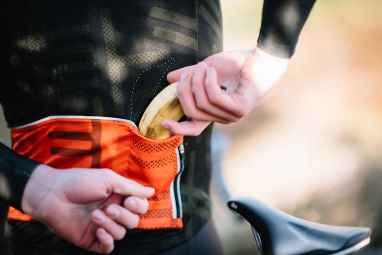 Hand slips a banana into the orange rear pocket of a Victory Chimp jersey, showing Banana Positioning Technology.
