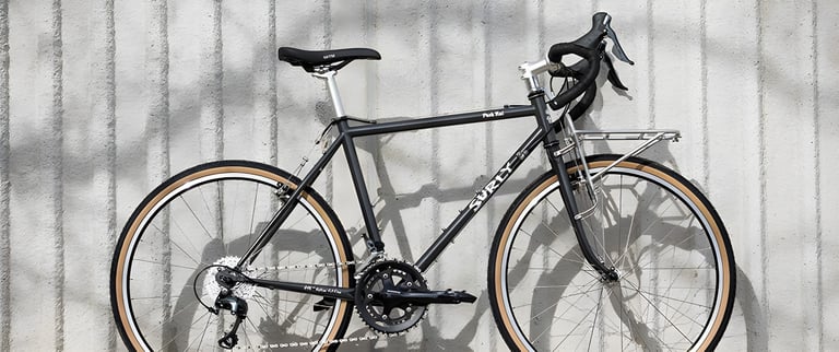 Surly Pack Rat in Grey Haze with tan-wall tyres and a silver front rack, side view.