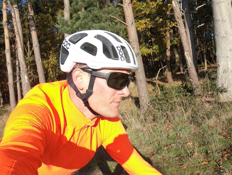 Rider in an orange jersey wearing the POC Octal helmet and dark glasses among pine trunks in low sun.