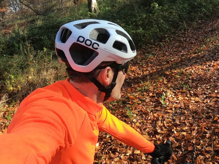 POC Octal helmet seen from behind the rider's shoulder on a leaf-covered track, chinstrap fitted.