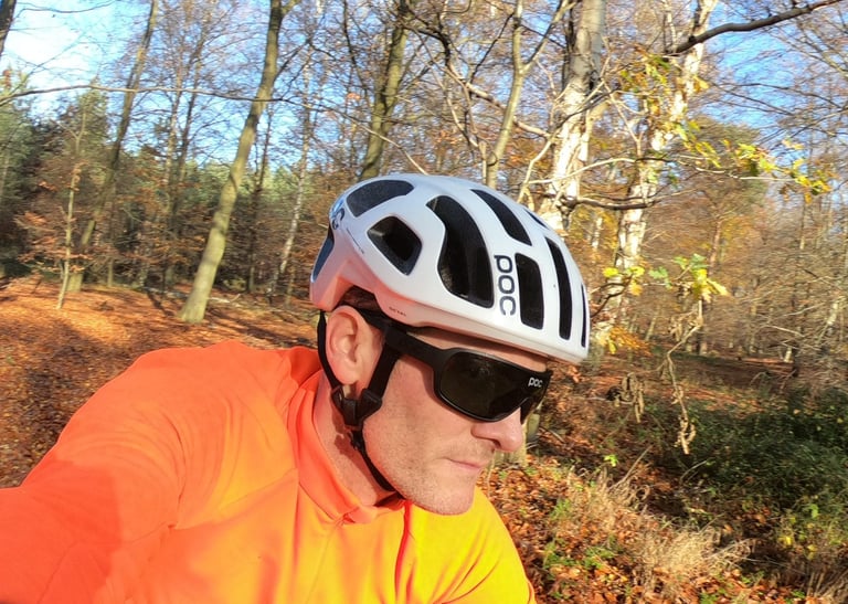 Rider in a bright orange top wearing the white POC Octal helmet and sunglasses in autumn woodland.