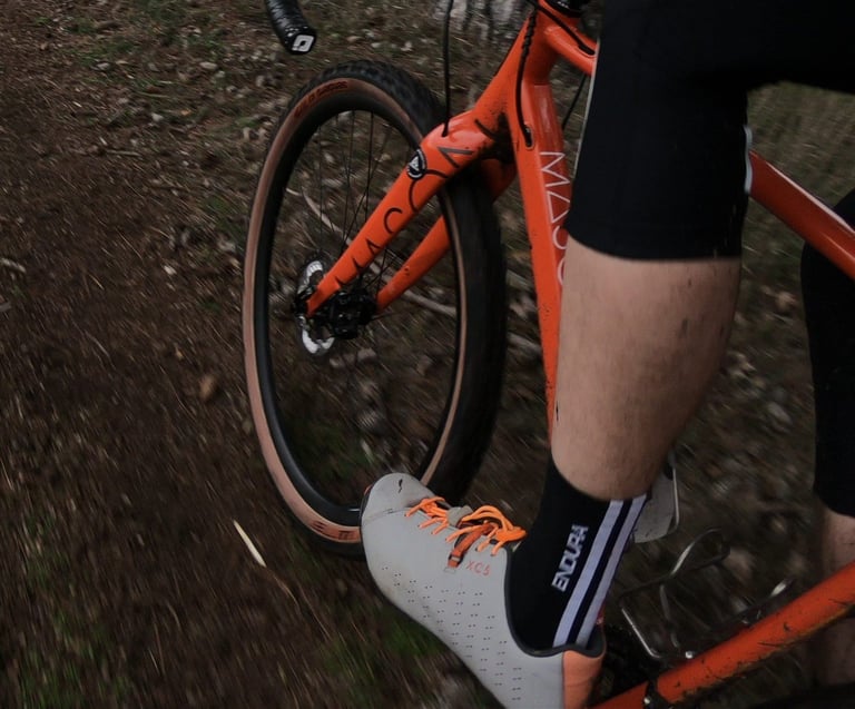 Rider pedalling an orange bike on a dirt trail, wearing Shimano XC5 shoes fitted with orange Lock Laces.