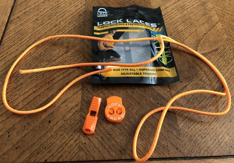 Contents of a Lock Laces packet: an orange elastic lace, a cord clip and a lace lock laid out on a wooden table.