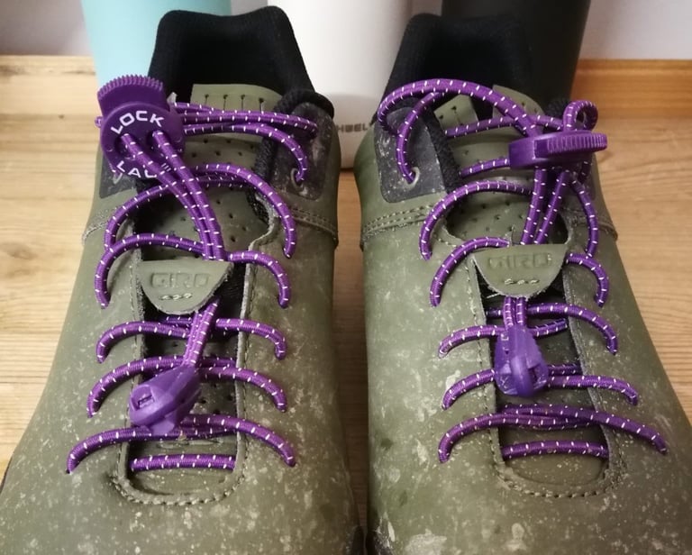 Pair of olive Giro shoes laced with purple Lock Laces, seen from the front with the lace locks at the top.
