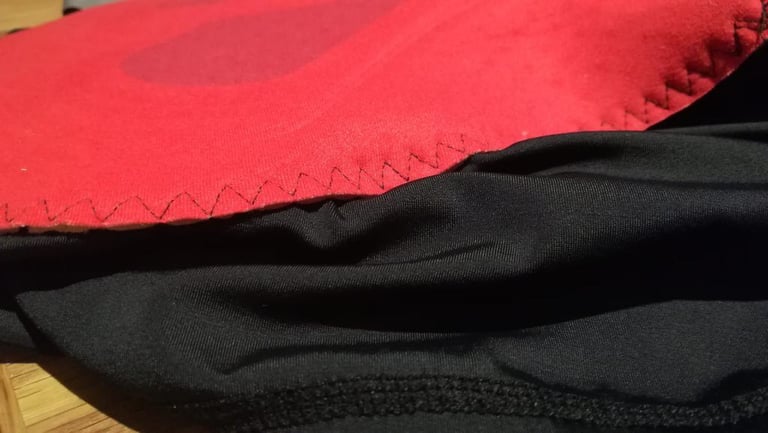 Close-up of the Alpkit Rhythm bibtights chamois edge with zigzag stitching on red pad and black fabric.