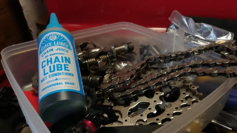 Juice Lubes Chain Juice Wet lube bottle beside a bike chain, cassette and pedal parts in a plastic tray.