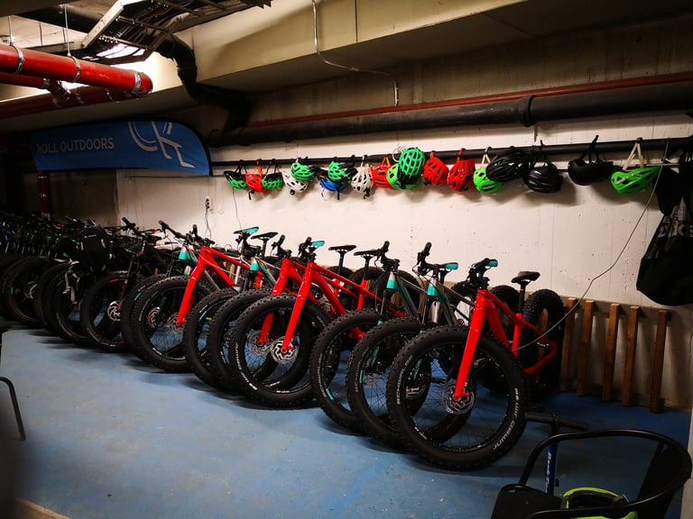 Roll Outdoors fatbike rental fleet racked in a Rovaniemi garage, red bikes with helmets hung on the wall behind.
