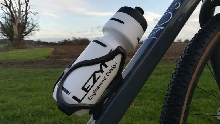 Side-on view of the Lezyne Flow Cage gripping a bottle on the down tube, with a knobbly gravel tyre alongside.