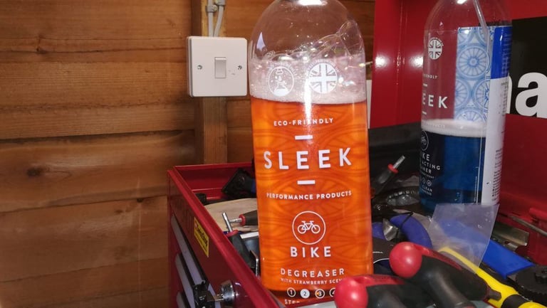 SLEEK Bike Degreaser bottle with frothy orange liquid, standing on a red workshop tool chest.