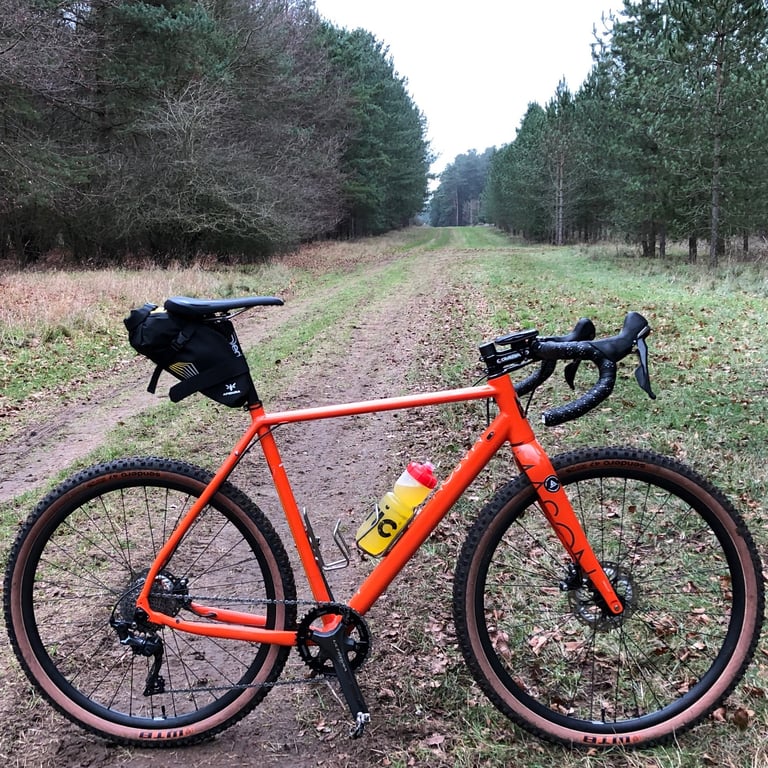 Mason Bokeh gravel bike on 650b WTB Sendero tyres, with saddle pack and bottle, on a grassy track between pine trees.