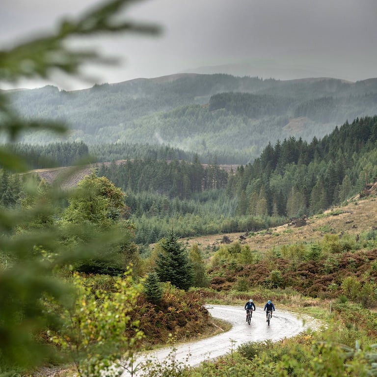 Two riders on a winding forest track below misty Trossachs hills, the kind of riding the Dukes Gold weekend promises.