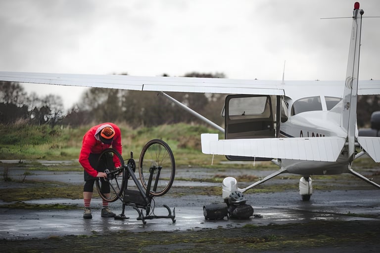 Toby works on the upturned Orange RX9 beside a light aircraft on a wet airfield, bags and helmet on the ground.