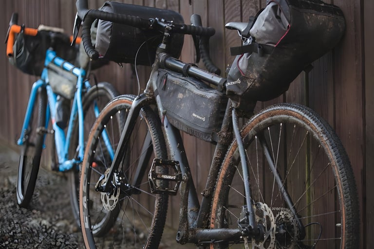 Mud-spattered Orange RX9 loaded with Blackburn bikepacking bags leans on a wooden fence beside a second bike.