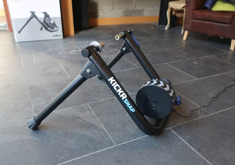 Wahoo KICKR Snap trainer unfolded on a slate floor, with its retail box behind.