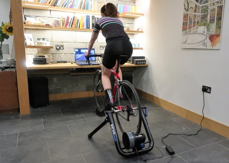 Rider pedalling on a Wahoo KICKR Snap indoor trainer in a home office, following Zwift on a laptop.
