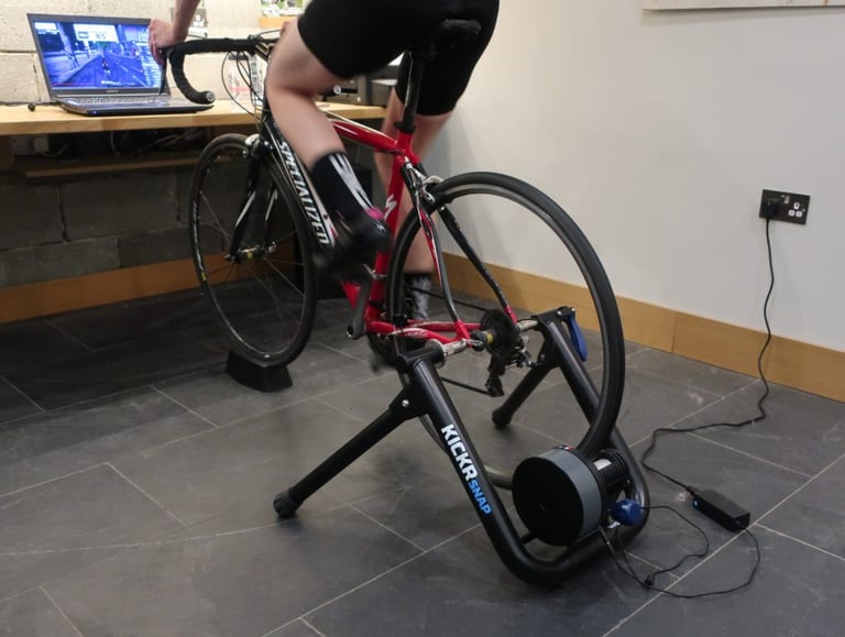 Specialized road bike mounted on a Wahoo KICKR Snap trainer, with a Zwift ride showing on the laptop behind.