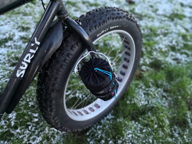 Black stuff sack held in a Passport Cycles Lug-Kage on a Surly fat bike fork, on frosty grass.