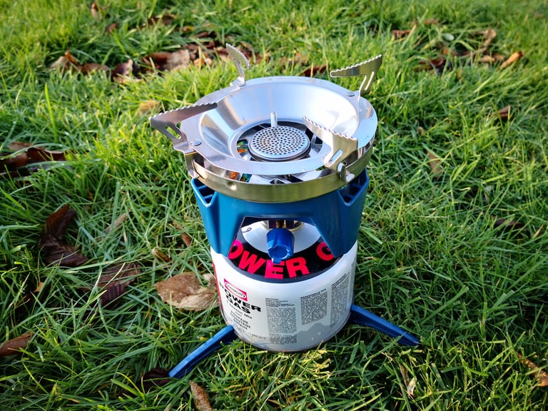 Alpkit BruKit burner with the pot adapter and canister tripod fitted on a gas canister, standing on grass.