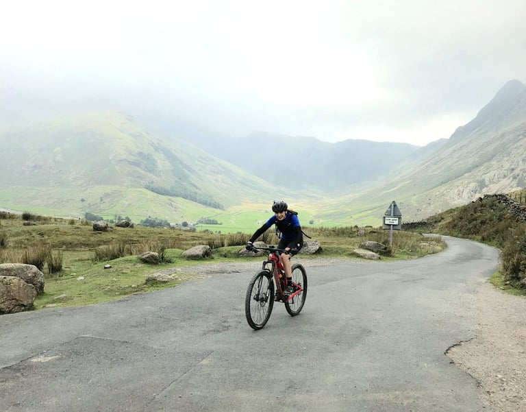 Rider on a mountain bike on a narrow road below mist-covered fells in the Lake District, venue for The Distance 2019.