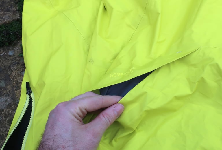Hand lifting the pass-through vent flap on the 7Mesh Rebellion jacket, beside the Gore-Tex Active label.