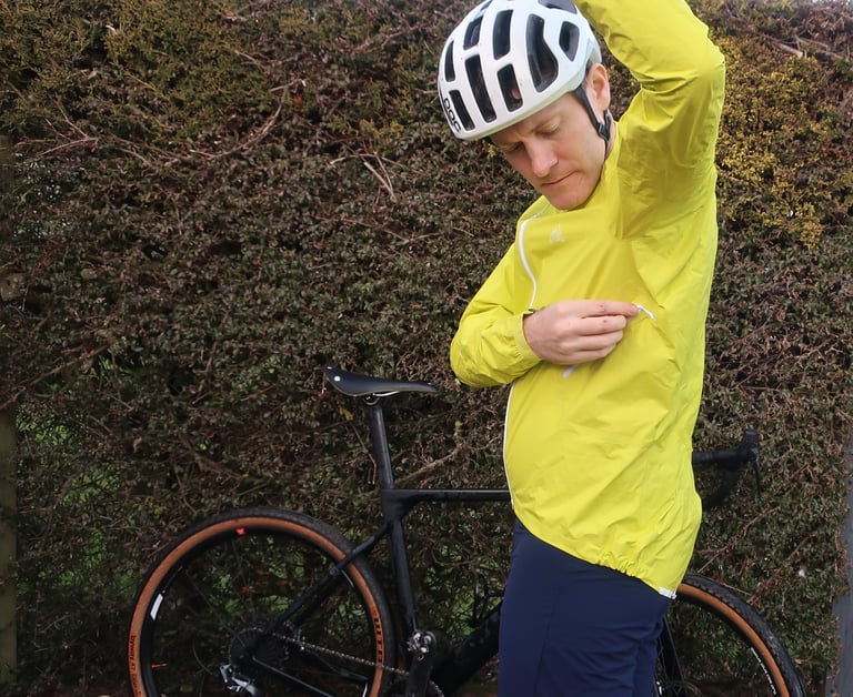 Rider in the 7Mesh Rebellion jacket reaching into the single zipped pocket under the left arm, bike behind.