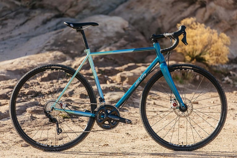 Complete All-City Cosmic Stallion 2019 with Shimano 105 groupset in new teal paint, parked on sandy ground by rocks.