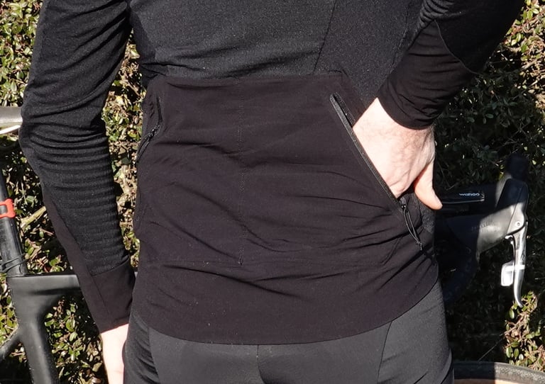 Rear of the 7Mesh Mission Jersey with a hand slipped into one of the two angled, zipped pockets.
