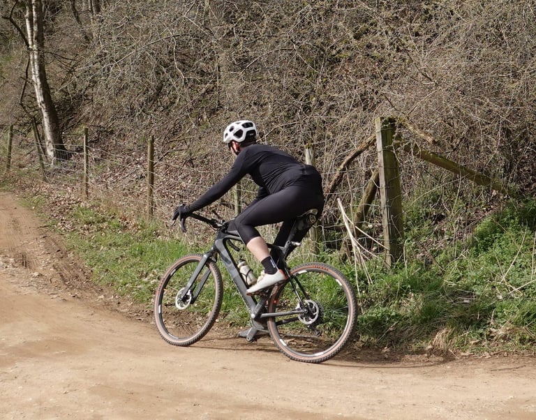 Rider in the black 7Mesh Mission Jersey climbs a dirt track on a gravel bike, seen from behind.