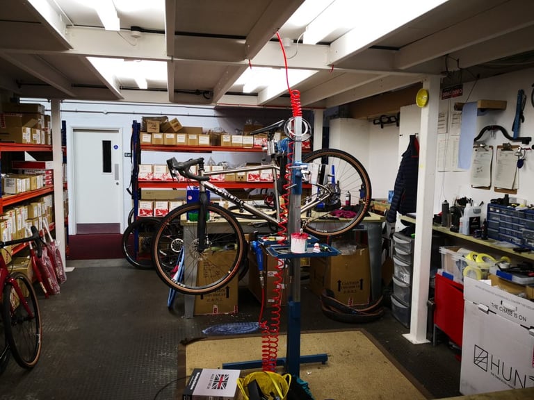 Titanium Sonder Camino clamped in a workstand among parts boxes in the Sonder workshop, with a Hunt wheels box in shot.