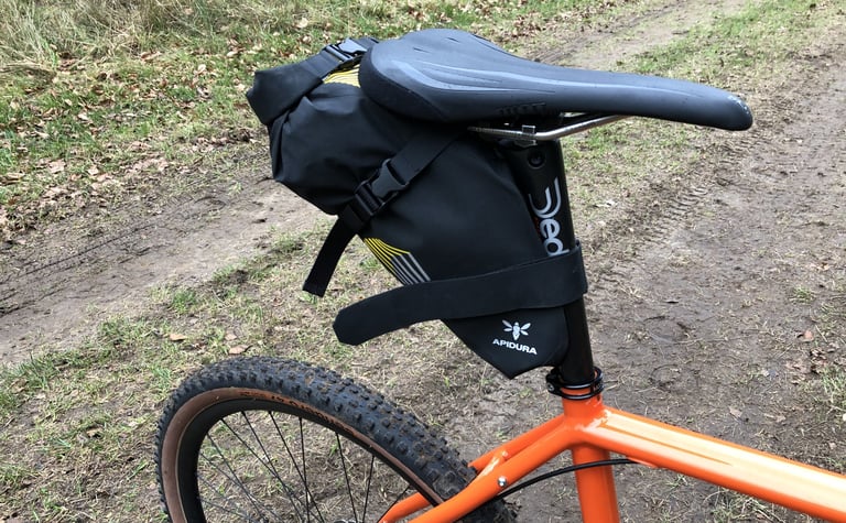 Apidura Racing Saddle Pack on an orange bike, showing its wide rubberised Velcro seatpost strap and buckles.