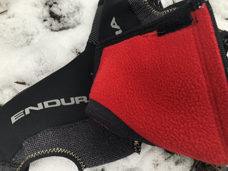 Red fleece lining inside an Endura Freezing Point overshoe, folded over beside the black neoprene outer on snow.