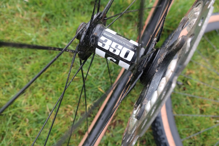 Close-up of a muddy DT Swiss 350 front hub on the Sharp Precision Wheels set, with rotor and spokes in the grass.