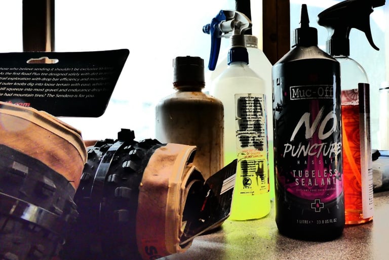 One-litre Muc-Off No Puncture Hassle tubeless sealant bottle on a bench among other workshop bottles and a knobbly tyre.
