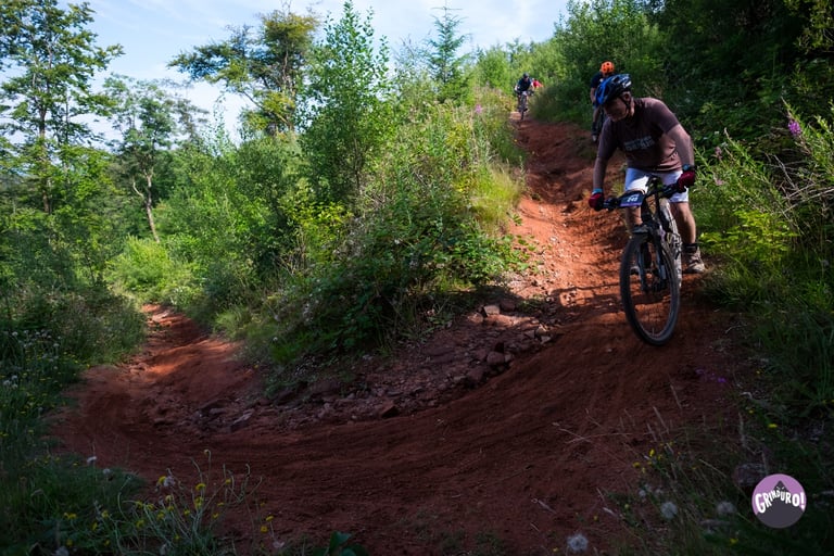 Rider descends a red dirt singletrack switchback through bracken on a Grinduro Scotland stage.