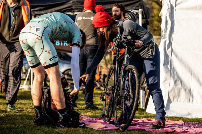A rider pulls on overshoes while another holds a gravel bike at sign-on for Yorkshire True Grit Dark Skies.
