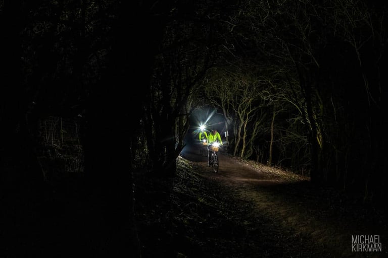 Two riders with bright lights on a dark woodland track during the night ride of Yorkshire True Grit Dark Skies.