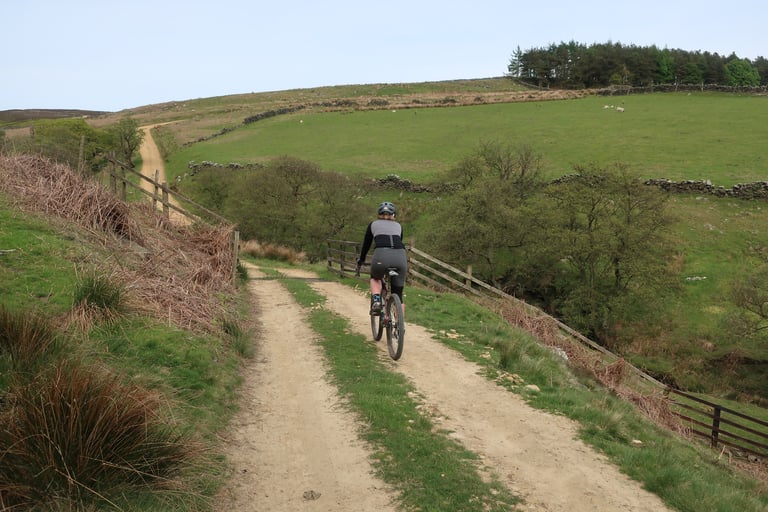 Rider on a gravel bike climbs a rough two-track bridleway past a wooden fence in the North York Moors.