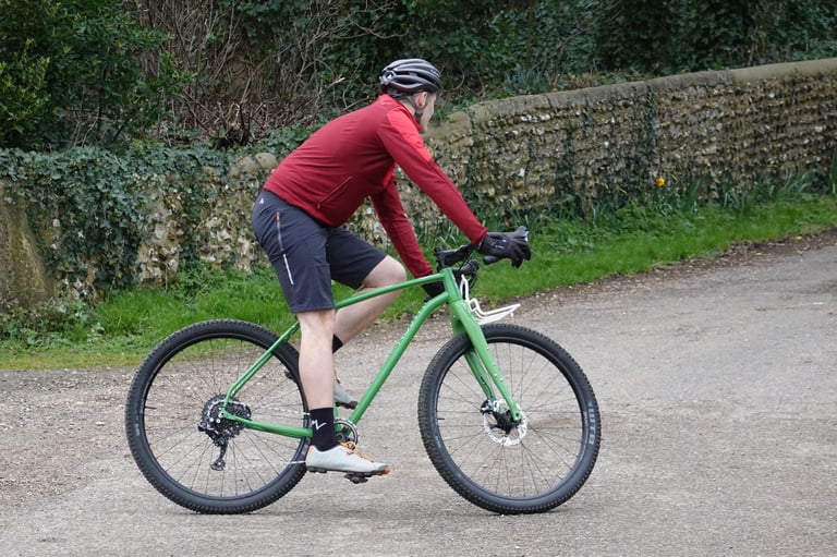 Rider in a red jacket on the Mason InSearchOf pedalling along a lane beside a flint wall.