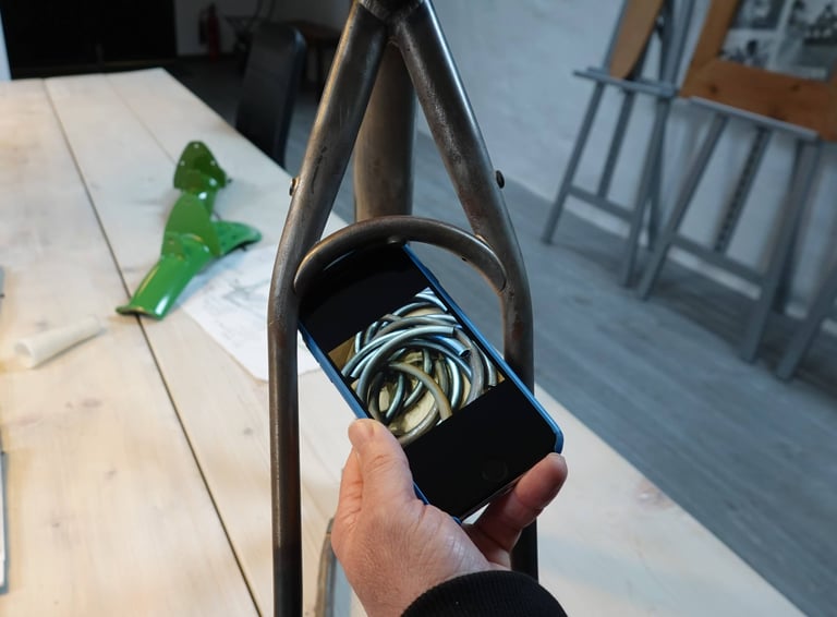 Hand holds a phone showing raw bent tubes in front of an unpainted Mason ISO seatstay bridge.
