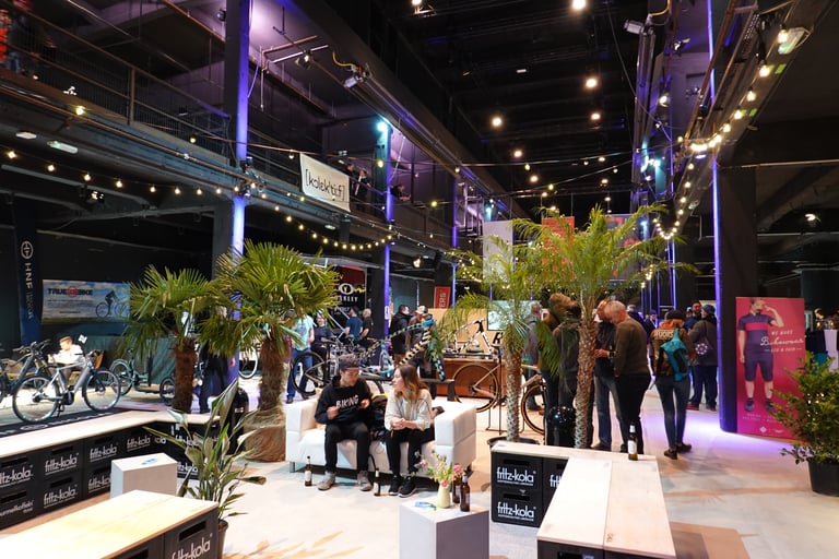 Seating among palm trees and fritz-kola crate benches inside the Kolektif Berlin Bike Fair venue.