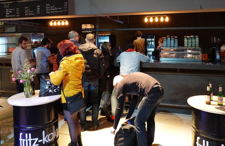Visitors queue at the bar at the Kolektif Berlin Bike Fair, with a coffee machine behind the counter.