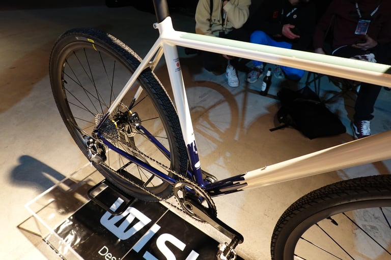 Close-up of the Wish One Gravel's white and blue steel frame, rear wheel, chainring and drivetrain.