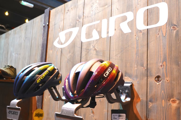 Two Giro Synth MIPS helmets in 2019 colours mounted on a wooden display wall under the brand's large white logo.