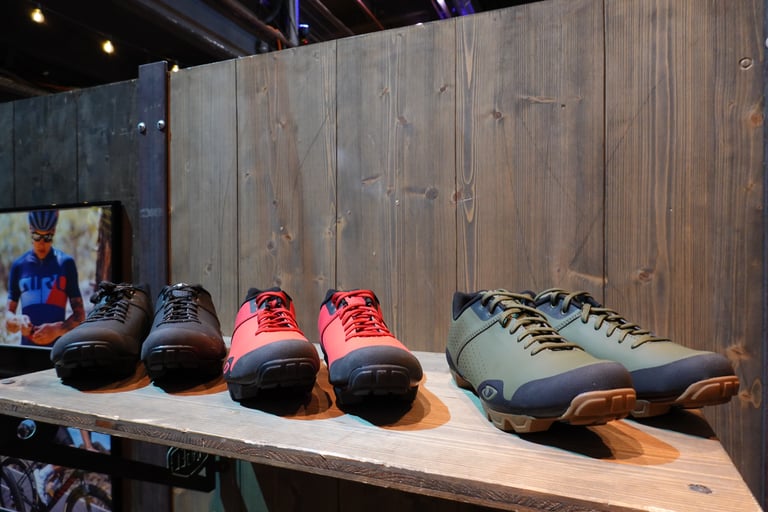 Giro SPD shoes in black, red and olive green on a wooden shelf at the Kolektif Berlin Bike Fair.